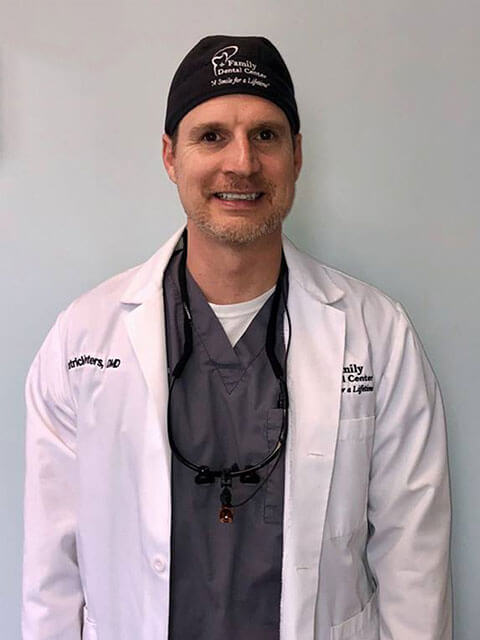 smiling man wearing dental scrubs and white coat